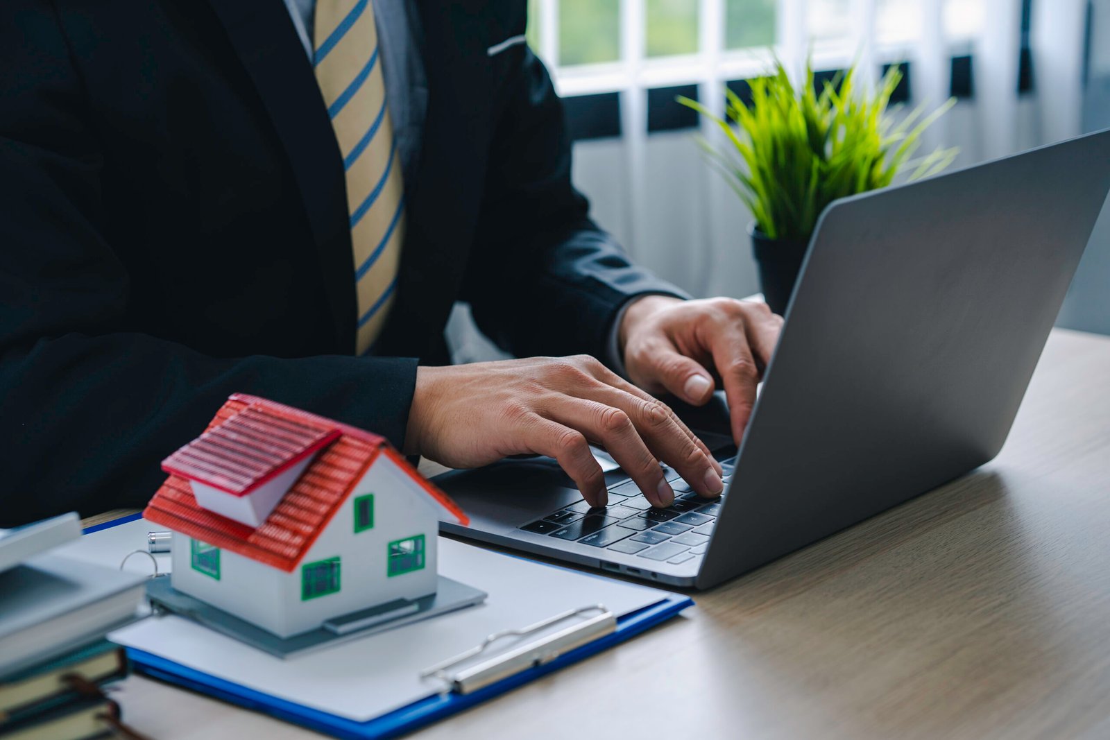 Licensed appraiser typing on laptop with model house and appraisal documents, representing Heritage Valuation Group's property appraisal services.